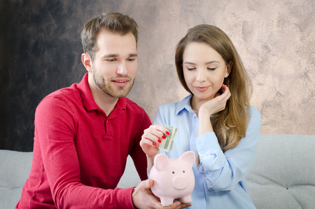 Young couple saves into piggybank. savings money couple piggybank home budget marriage cost conceptの写真素材