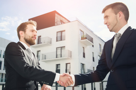 Two men are standing on the balcony and shaking hands. Investor or customer buying apartmentの写真素材