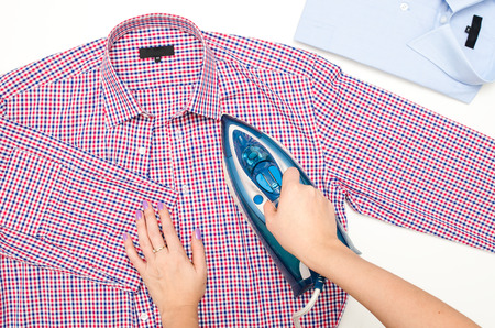 Female hand ironing men's shirt. Blue iron on white background top view.の写真素材