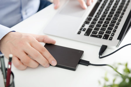 External backup disk hard drive connected to laptop. Man with notebook making safety personal data...