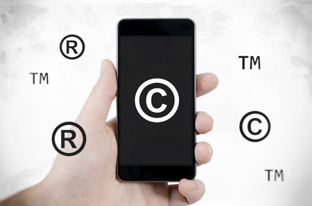 Copyright, trademark symbols flying around smartphone. Security and piracy composition. Dirty noise styleの写真素材