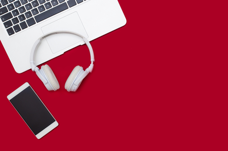 Office desk table with laptop, smartphone, and headphones. Flat lay with copy space on red backgroundの写真素材