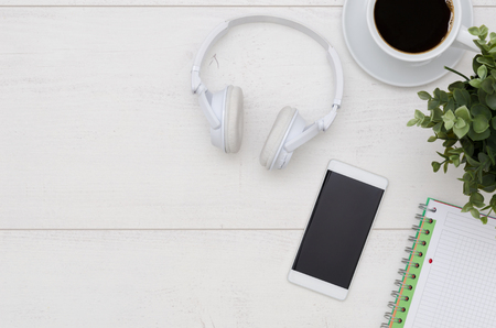 Office desk table with phone, headphones, and supplies. Flat lay with copy space on white wooden backgroundの写真素材