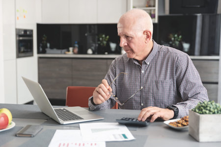 Senior man doing some paperwork and calculations at home. Pensioner counts money, tax calculation conceptの写真素材