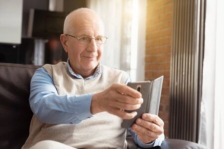 Senior man using a smartphone and smiling while sitting on couch at home.の写真素材
