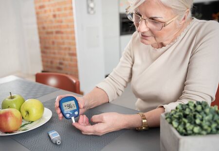 Senior woman with glucometer checking blood sugar level at home. Diabetes, health care conceptの写真素材