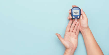 Man using glucometer, checking blood sugar level. Wide image with copy space, blue background. Diabetes conceptの写真素材