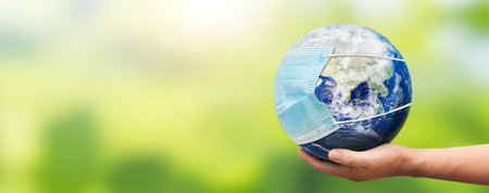 Hand holding Earth globe with face mask. World pandemic concept.の写真素材
