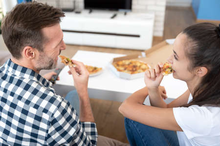 Couple watching TV while eating pizza. Spending free time at homeの写真素材