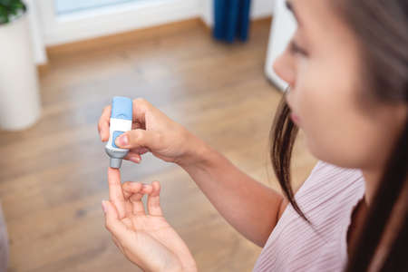Woman using lancet for diabetes. Hypoglycemia, blood sugar level control at homeの写真素材