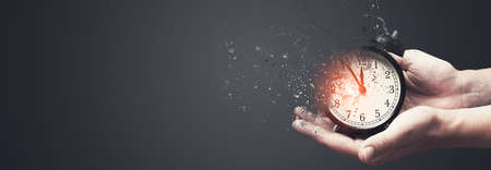 Concept of passing away, the clock breaks down into pieces. Hand holding analog clock with dispersion effectの写真素材