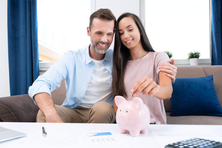 Hand putting coin to piggy bank. Young couple is saving money for their new home.の写真素材