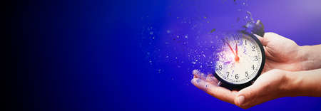 Concept of passing away, the clock breaks down into pieces. Hand holding analog clock with dispersion effectの写真素材