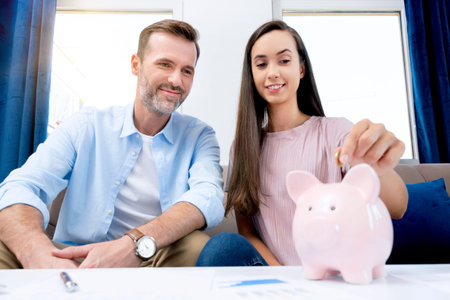 Hand putting coin to piggy bank. Young couple is saving money for their new home.の写真素材