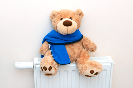 Radiator at home, the concept of rising heating prices. Teddy bear with a scarf sits on a radiator