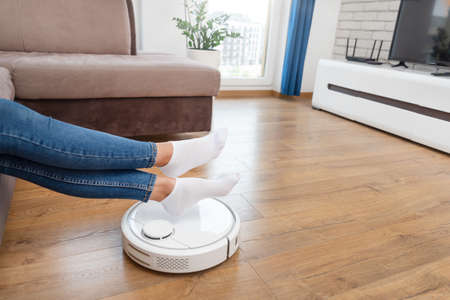 Robotic vacuum cleaner cleaning the room, legs raised up. Smart home conceptの写真素材
