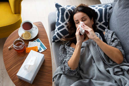 Sick woman blows her nose into a handkerchief, lying on bedの写真素材