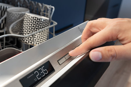 Man pushing start button on the control panel of the dishwasher.