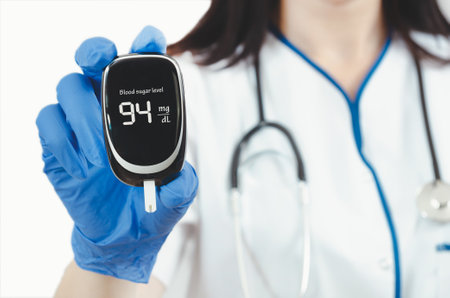 Doctor holding a glucose meter with a reading of 94 mg/dL. Concept of professionalism and expertise, as the doctor is wearing a white lab coat and glovesの写真素材