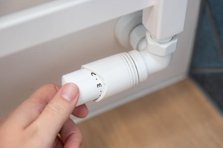 Person is adjusting the temperature on a radiator. The radiator is white and has a knob on itの写真素材