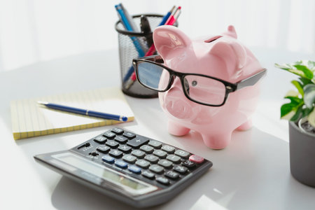 Smart piggy bank wearing glasses, using calculator, calculating financesの写真素材