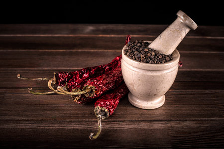 marble mortar with spices black pepper and red hot pepper on a wooden table