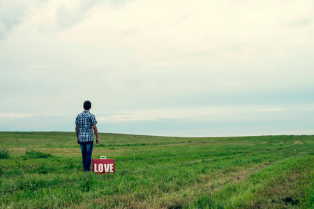 the guy stand in the field in which hands a suitcase with a text "love"の写真素材