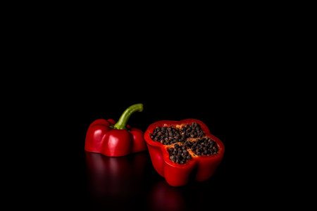 red paprika cut in two with dry black pepper inside on black の写真素材