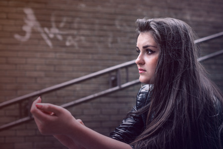 serious girl sits on street ladder against  brick wall