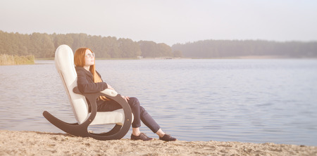 beautiful happy woman has a rest in chair on bank of the lake morningの写真素材
