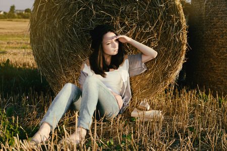 beautiful girl hipster looks in distance against hay bale in fallの写真素材