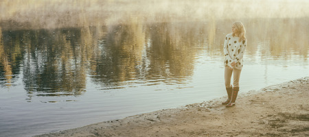 lonely beautiful girl walks on river bank early in the morningの写真素材