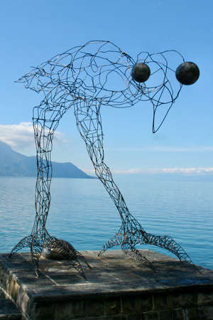 Wire line art huge bird figurine with big eyes over water through high mountains. Big bird looking deep into the camera. Open skies with few clouds around the top of the mountain.の写真素材