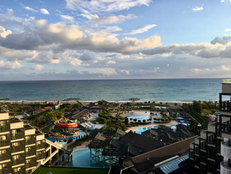 Panaromic view of beautiful shore and touristic facilities. Swimming pool, sea, beach, cloudy dramatic sky, sunlight and shadows, restaurant and cafe.のeditorial素材
