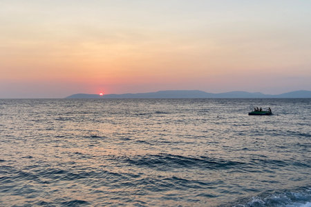 Sunset on the Aegean Mediterranean sea with pine trees sun down behind mountains on the horizon. People swimming and on floating pontoon. Great holiday, tourism, tranquil, luxury.の写真素材