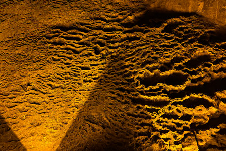 Cave wall with light, interior of the beautiful cave, abstract background and texture, stalactites and stalagmites, underground, natural water shaped wallsの写真素材