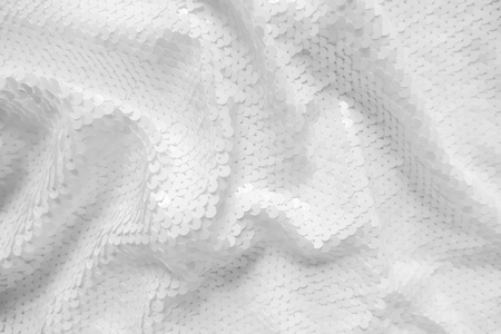 Background sequin. Holiday abstract glitter background with blinking lights. Fabric sequins in white color. Fashion fabric glitter.の写真素材