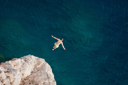 Young man jumping from cliff into sea.