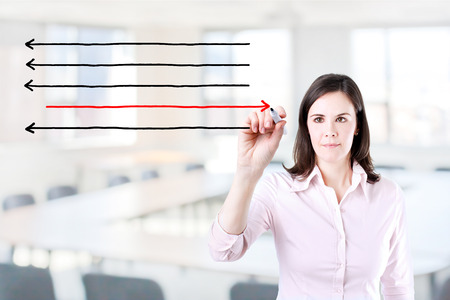 Businesswoman drawing arrows in different directions. Office background.の写真素材