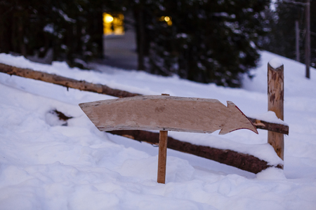 Wooden direction sign with less snow on it and with snowfall and mountains on backgroundの写真素材