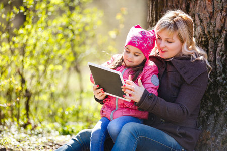 Mother and daughter using digital tablet while sitting in the beautiful nature,Mother and daughter...