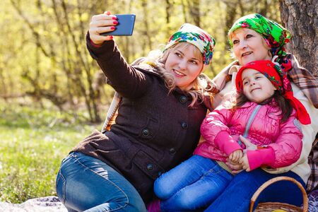 Three generations of women. Beautiful granny, mother and daughter are doing selfie and smiling while sitting on couch at home mom daughter grandmother selfieの写真素材