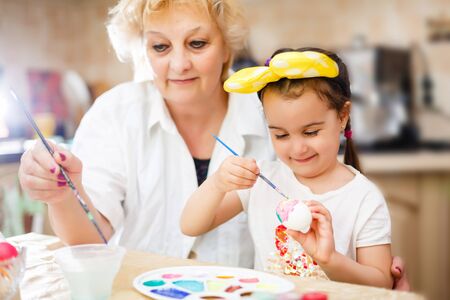 Grandmother with granddaughter are coloring eggs for Easter. white, t-shirt, brushesの写真素材