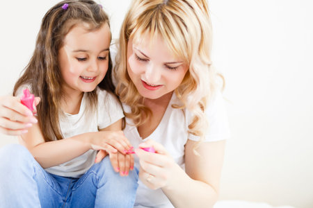 Mom and daughter in the bedroom on the bed in the curlers make up, paint their nails and have fun Mom paints nails to my daughter on the bedの写真素材