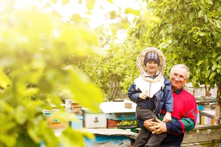 Experienced beekeeper grandfather teaches his grandson caring for bees. Apiculture. The concept of transfer of experienceの写真素材
