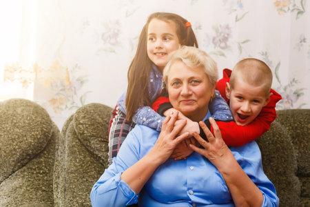 Grandmother and grandchildren sitting together on sofa in living roomの写真素材