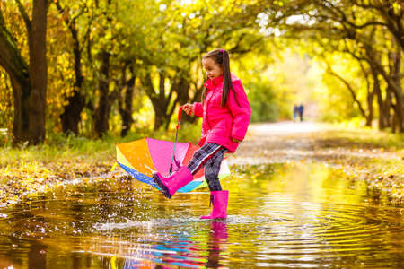 Adorable toddler girl with colorful umbrella outdoors at autumn rainy dayの写真素材