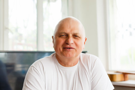 Head shot close up happy grandfather looking at camera, talking to grown up children or communicating via video call with friends, sitting on sofa at home. Pleasant old man involved in conversation.の写真素材