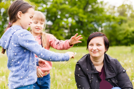 Mother with small daughter blowing to dandelion - lifestyle outdoors scene in parkの写真素材