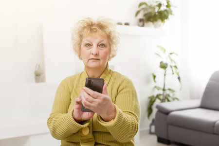 Upset elderly woman using touch screen mobile for taking selfie or making video callの写真素材